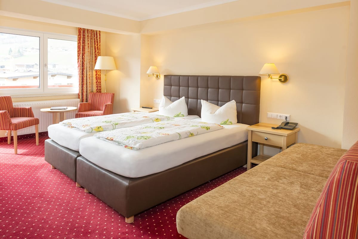Une chambre d’hôtel avec un lit double, deux tables de chevet, une chaise, une petite table ronde et une fenêtre avec des rideaux.