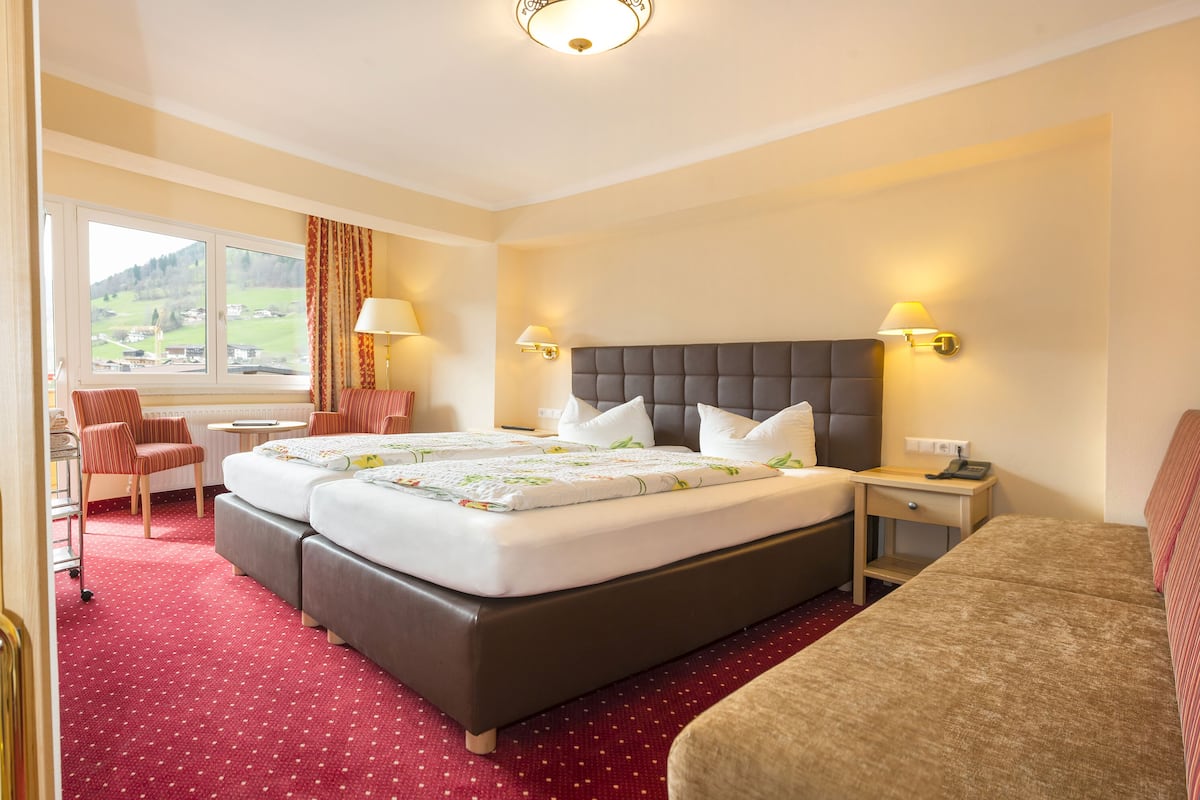 Une chambre d’hôtel avec un grand lit, deux tables de chevet, un bureau, une chaise et une fenêtre donnant sur la campagne.