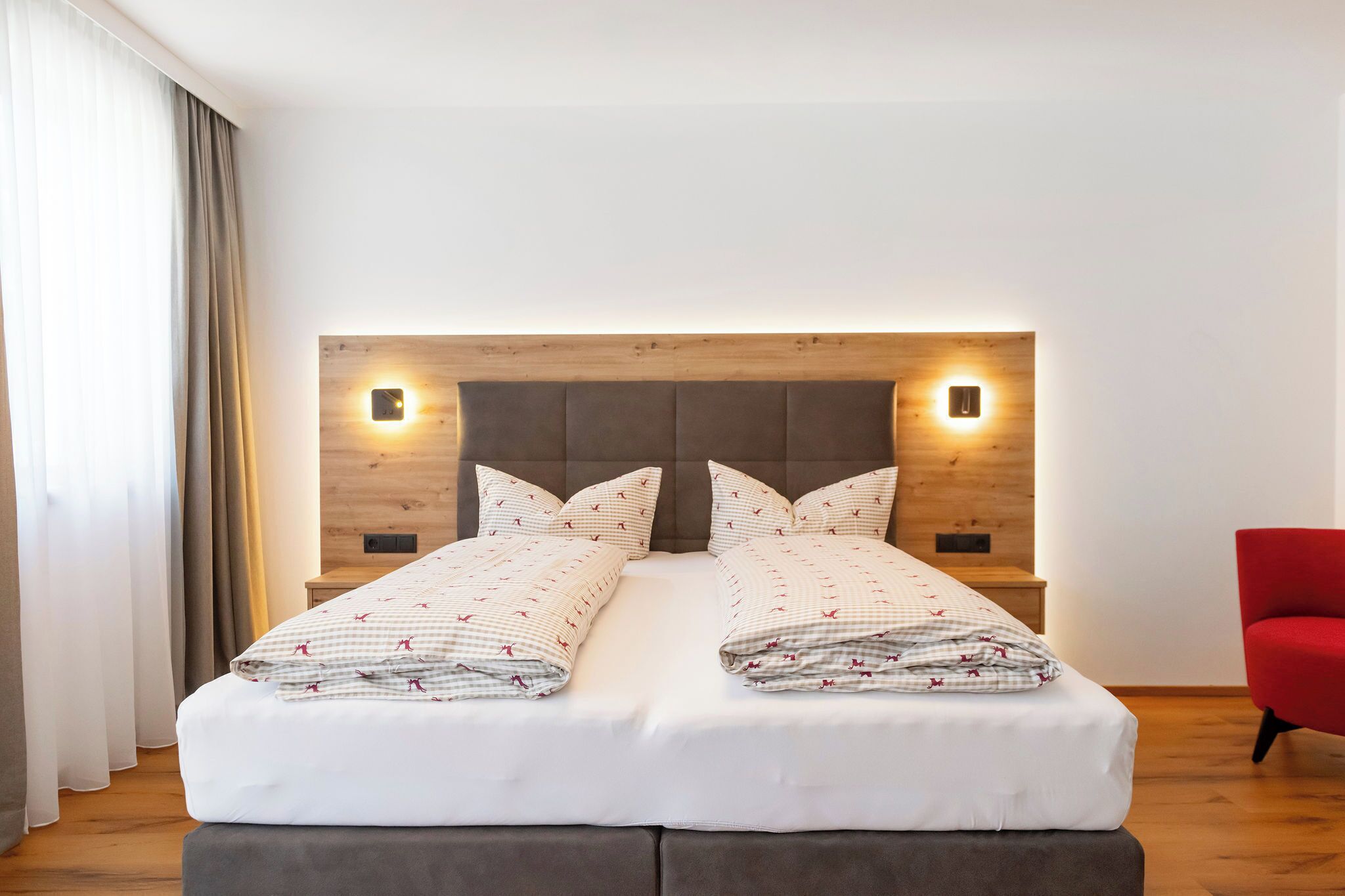 Un lit double avec une tête de lit en bois, deux tables de chevet et une chaise rouge.