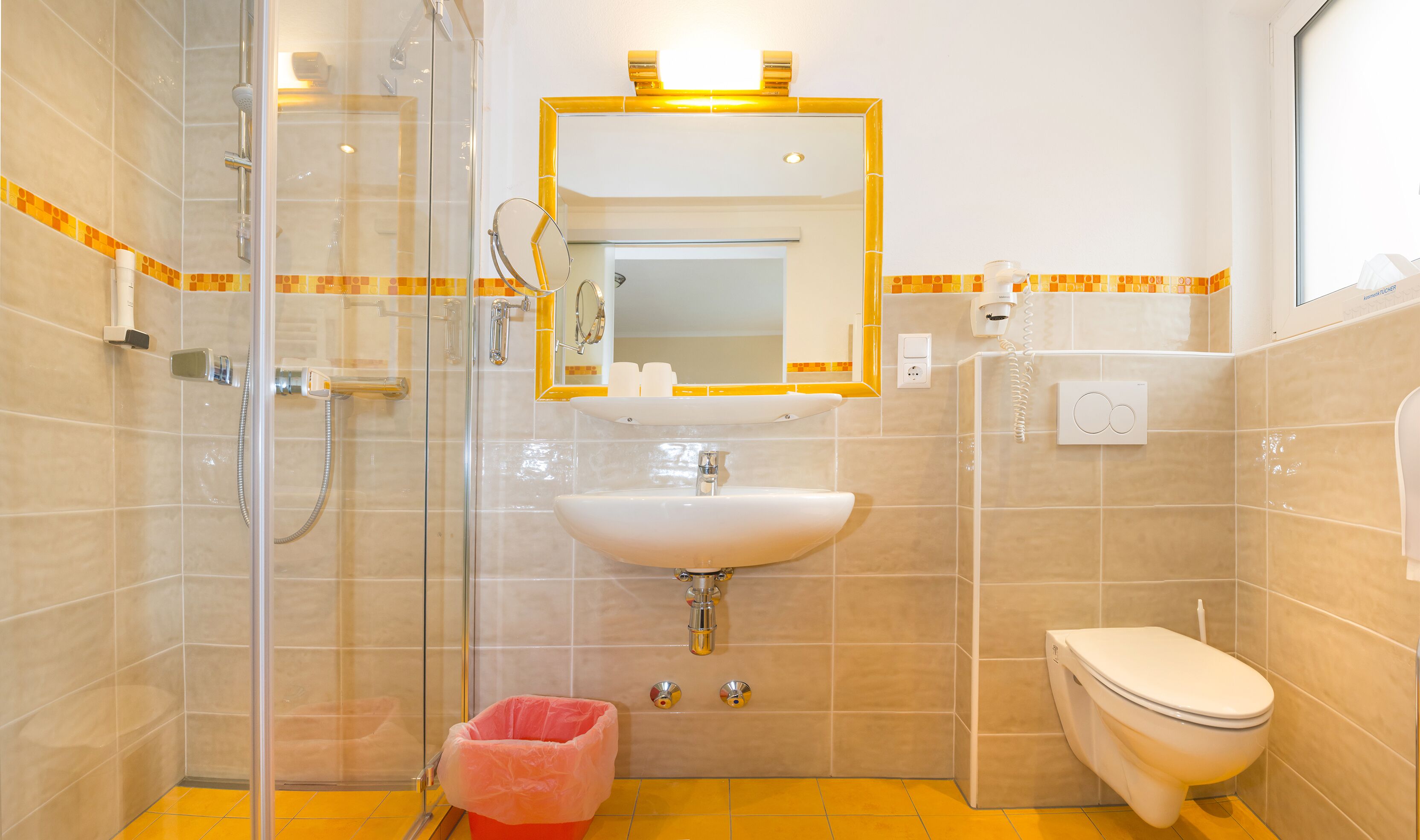 Un baño con cabina de ducha de vidrio, lavamanos, inodoro y espejo con marco dorado.