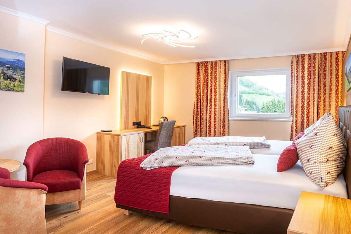 Une chambre d’hôtel avec un lit, un bureau, une chaise, une télévision et une fenêtre avec des rideaux.