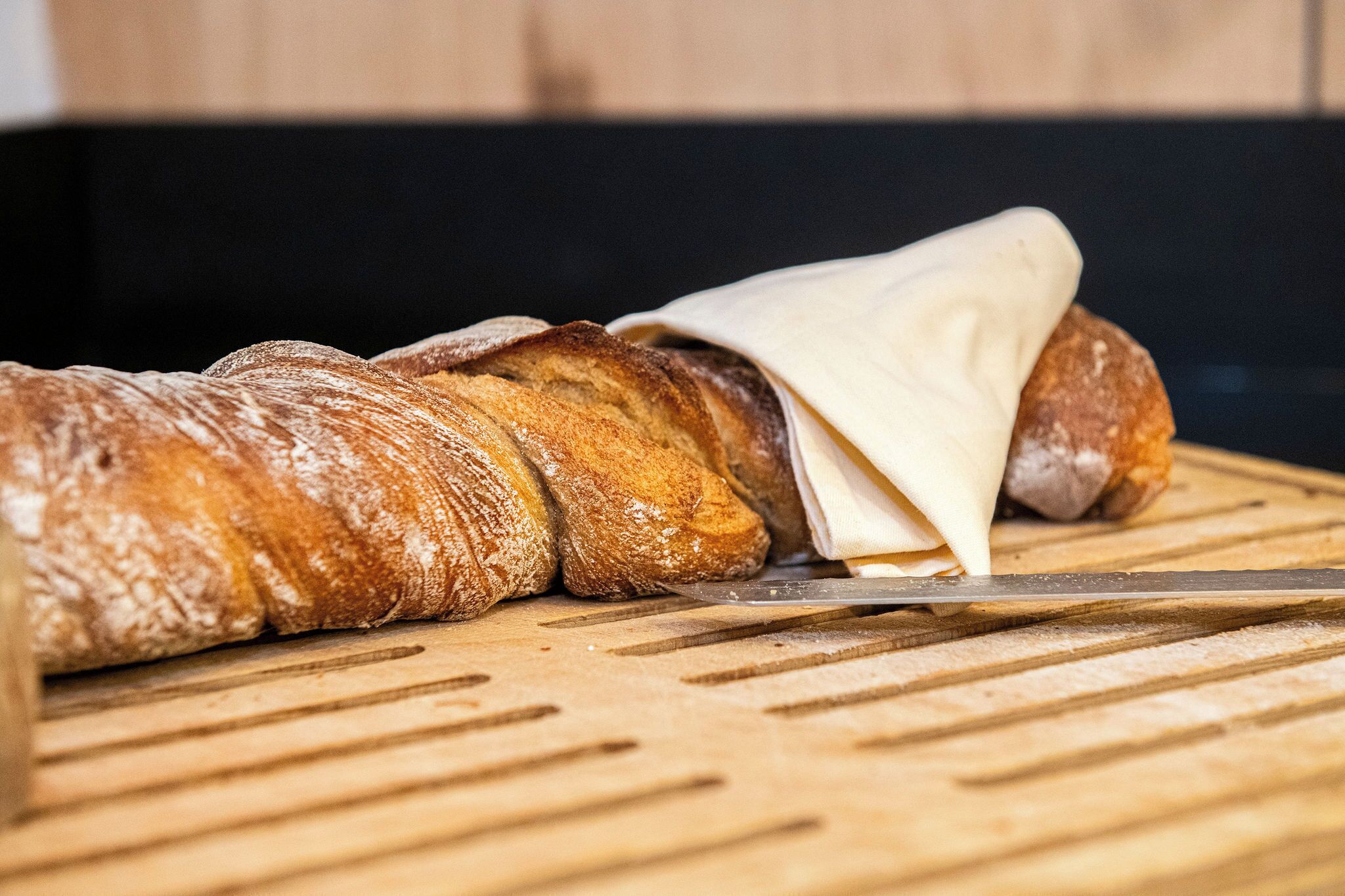 A loaf of bread being sliced on a wooden cutting board.