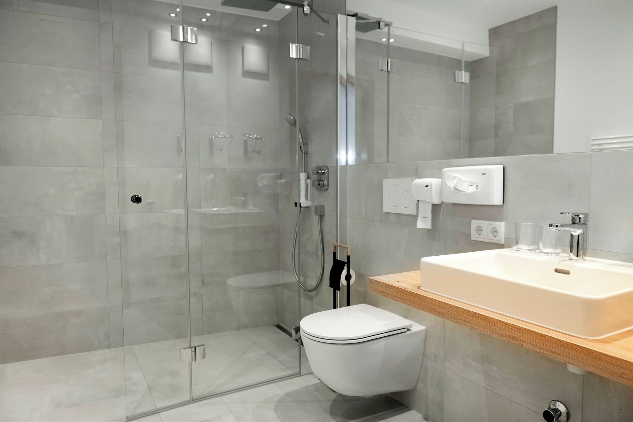Une salle de bain moderne avec une douche à parois de verre, des toilettes blanches et un meuble-lavabo en bois avec un évier.