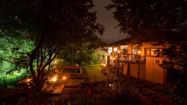 Un espacio exterior bien iluminado con una terraza de madera, una piscina pequeña y una escalera que lleva a un edificio.