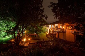 Un espacio exterior bien iluminado con una terraza de madera, una piscina pequeña y una escalera que lleva a un edificio.