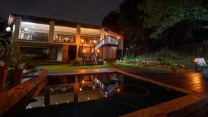Una casa moderna de dos pisos con piscina, iluminación exterior y una escalera que conduce al nivel superior.