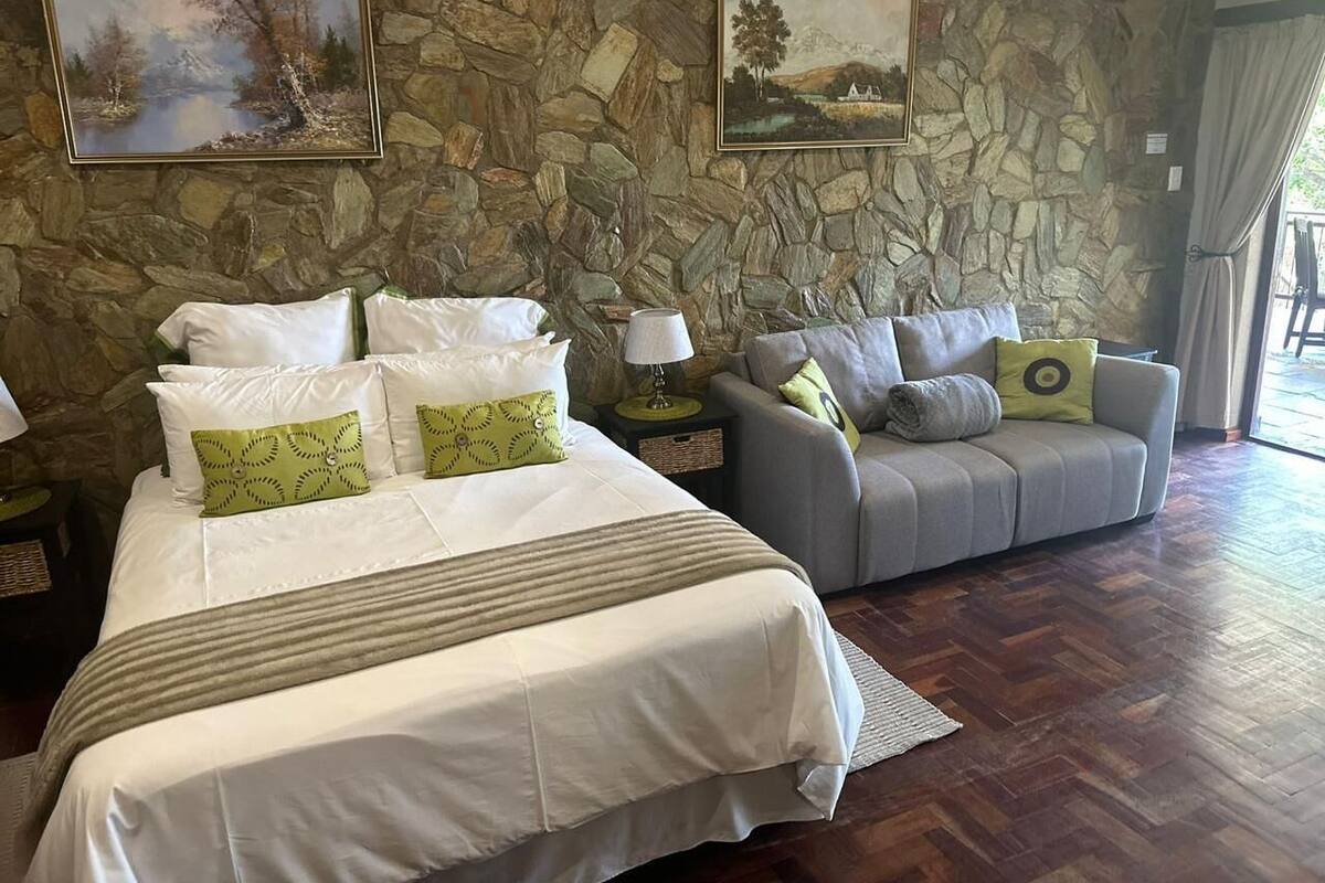 A bedroom with a large bed, a grey sofa, stone walls, and two paintings.