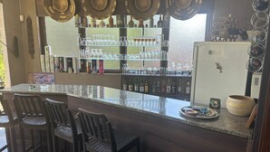 Una zona de bar con encimera de granito, varios estantes con cristalería y un refrigerador.