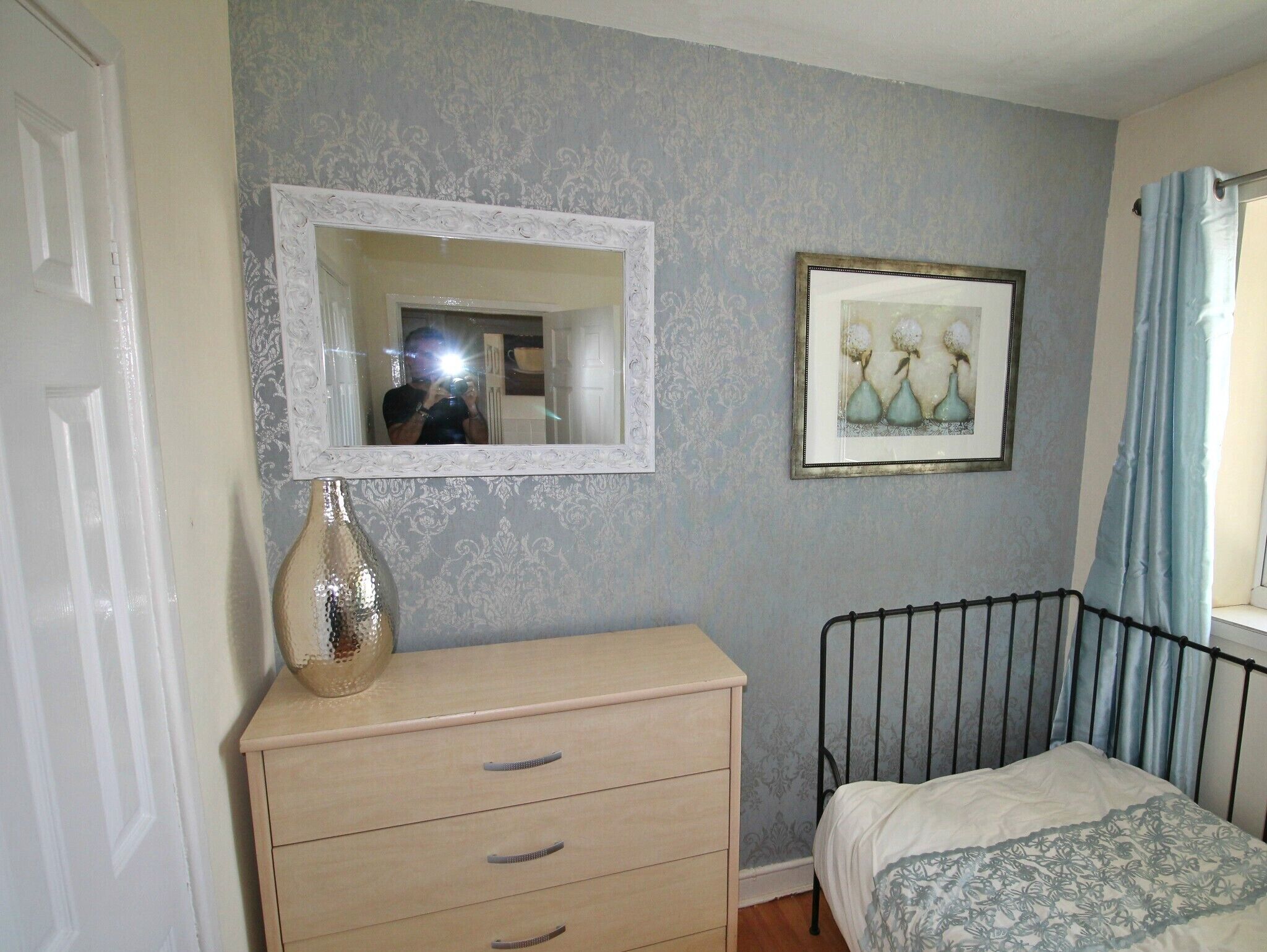 Una camera da letto con un letto, una cassettiera, uno specchio e un quadro appeso al muro.