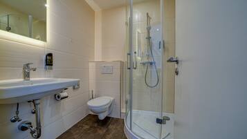 Een moderne badkamer met een douchecabine van glas, een witte wastafel en een toilet.