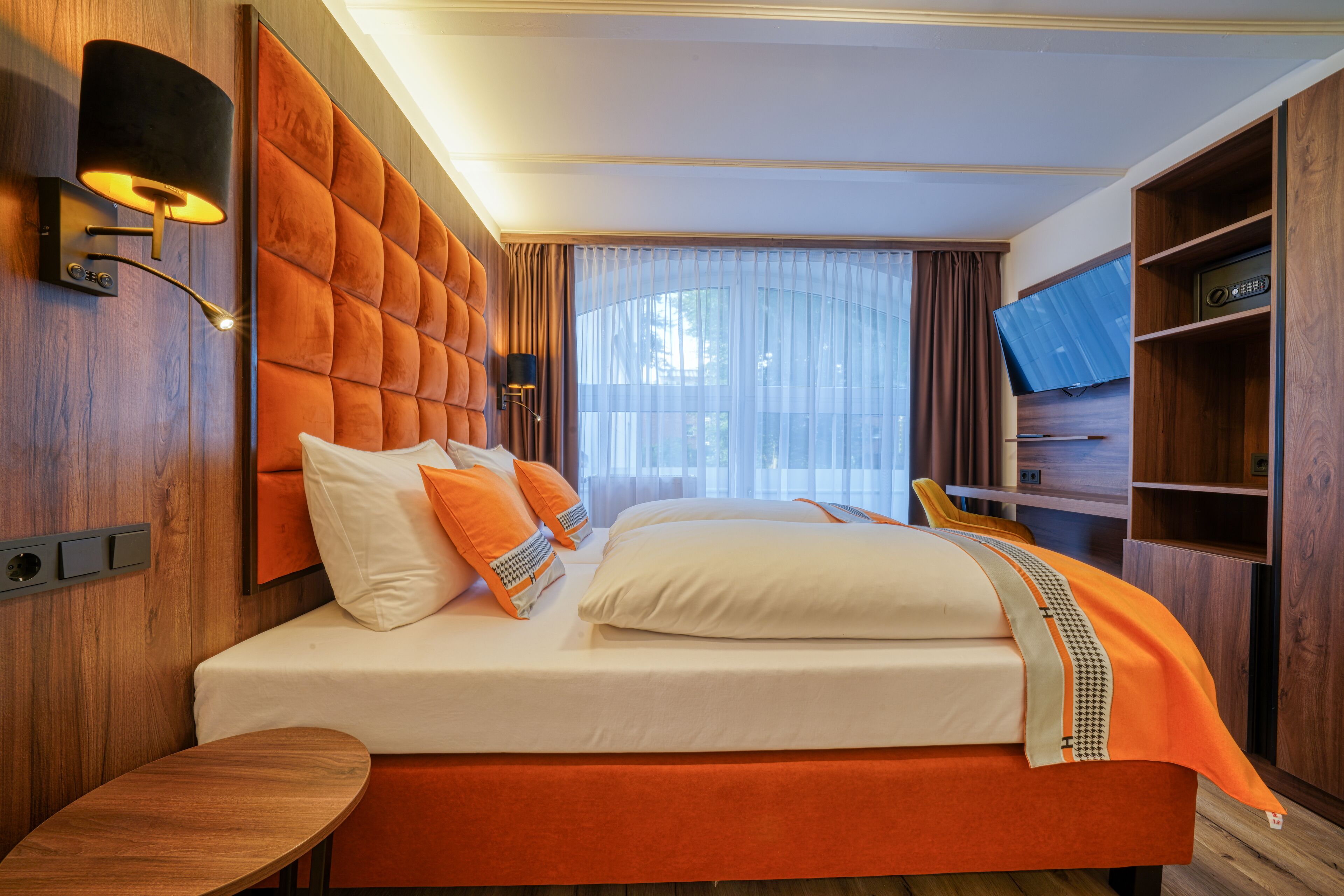 Une chambre d’hôtel avec un grand lit, une table de chevet, un téléviseur fixé au mur et une tête de lit en bois.