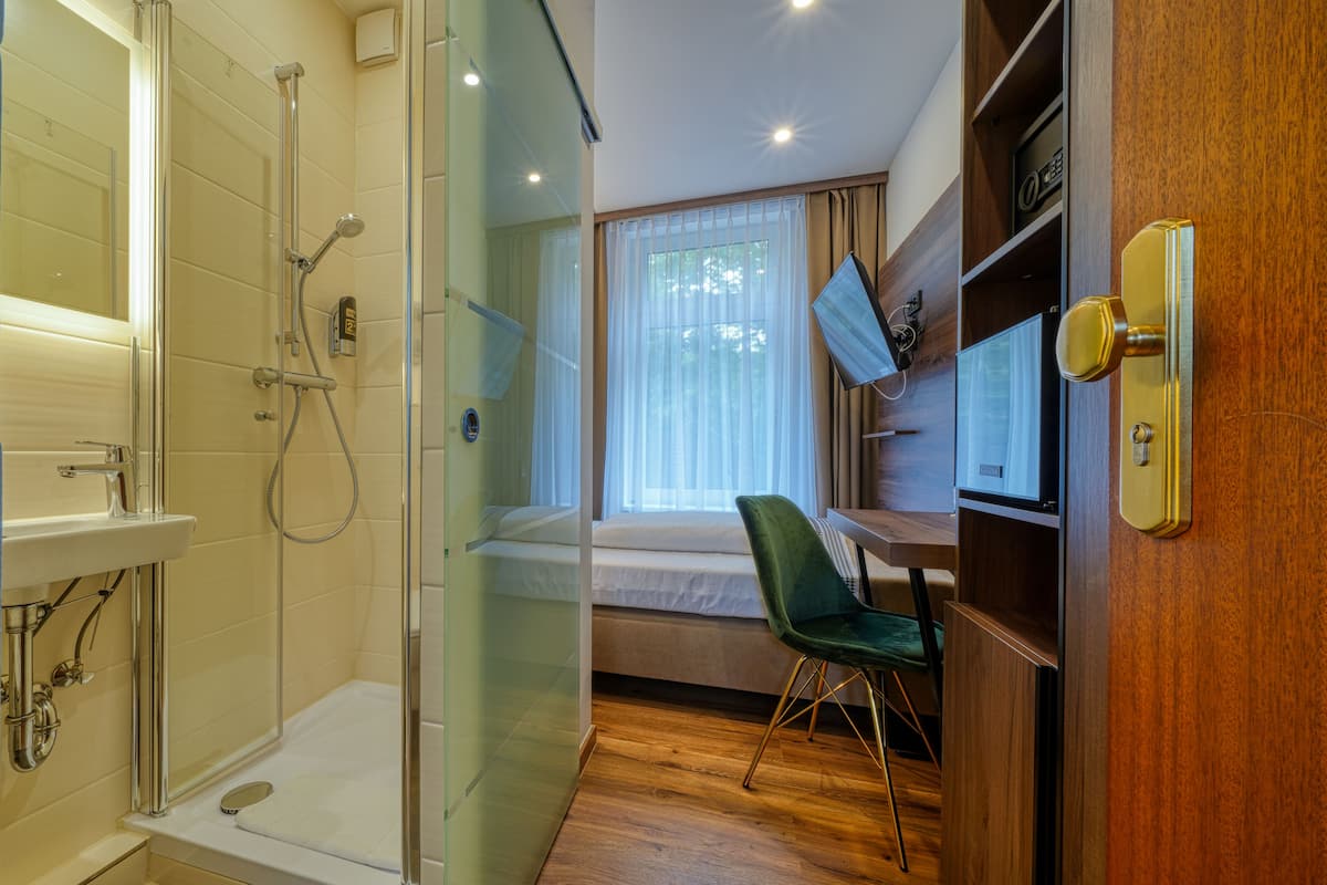Habitación de hotel con cabina de ducha de vidrio, cama con vistas al exterior, escritorio con silla y televisor.