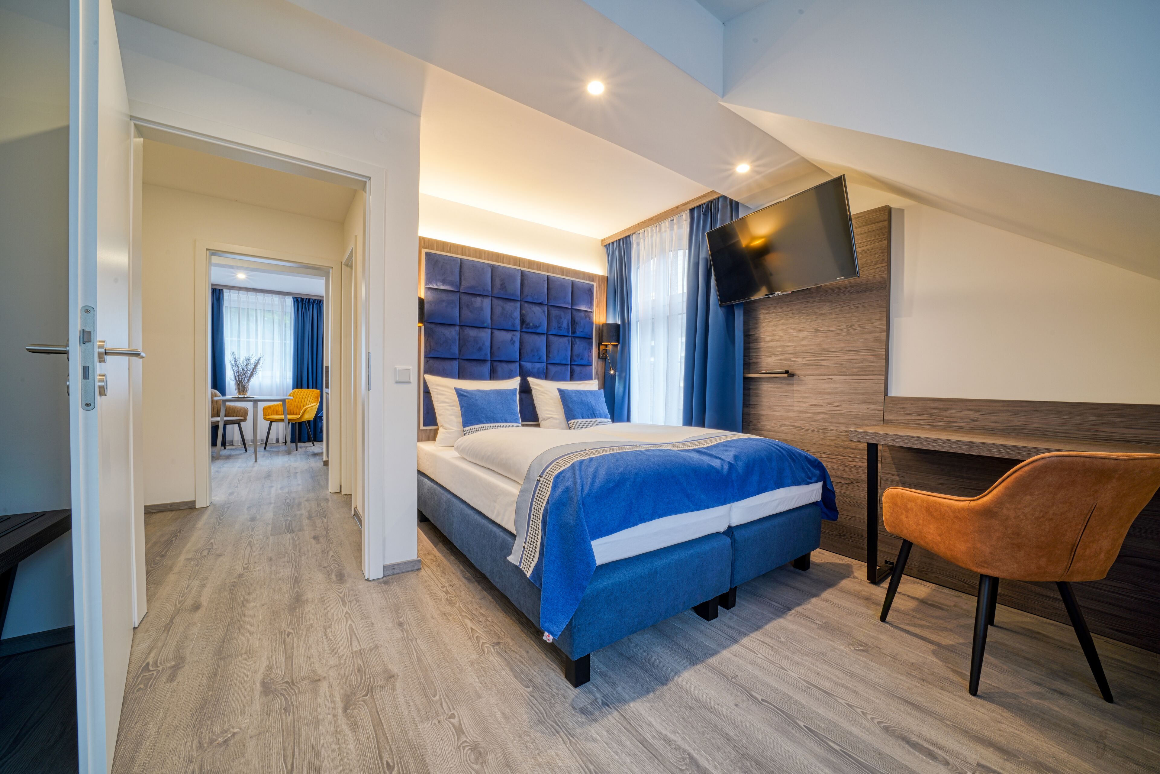 Una habitación de hotel moderna con una cama grande, un escritorio, un televisor y un rincón de comedor con sillas.