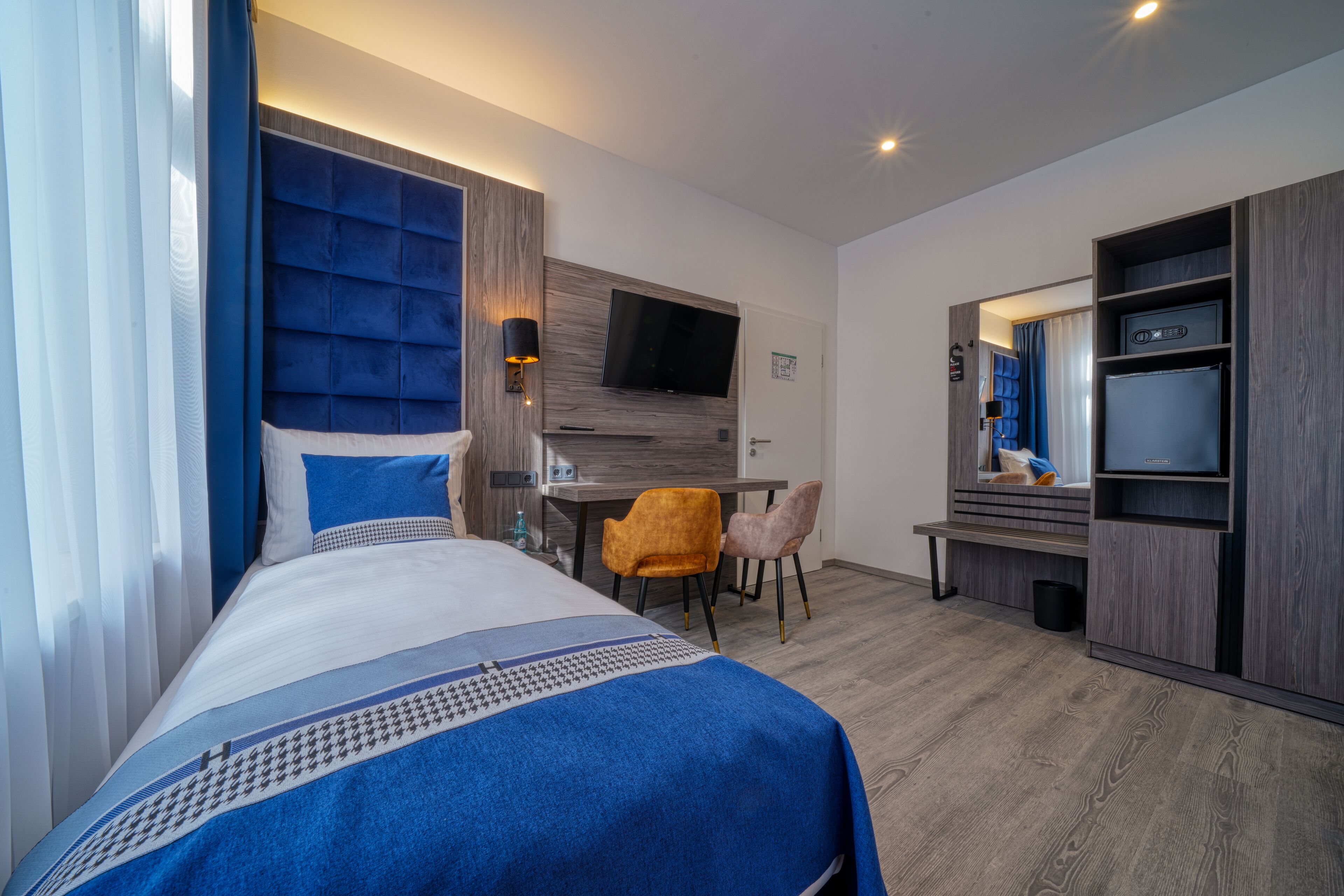 Una habitación de hotel moderna con una cama grande, un escritorio, un televisor y un armario.
