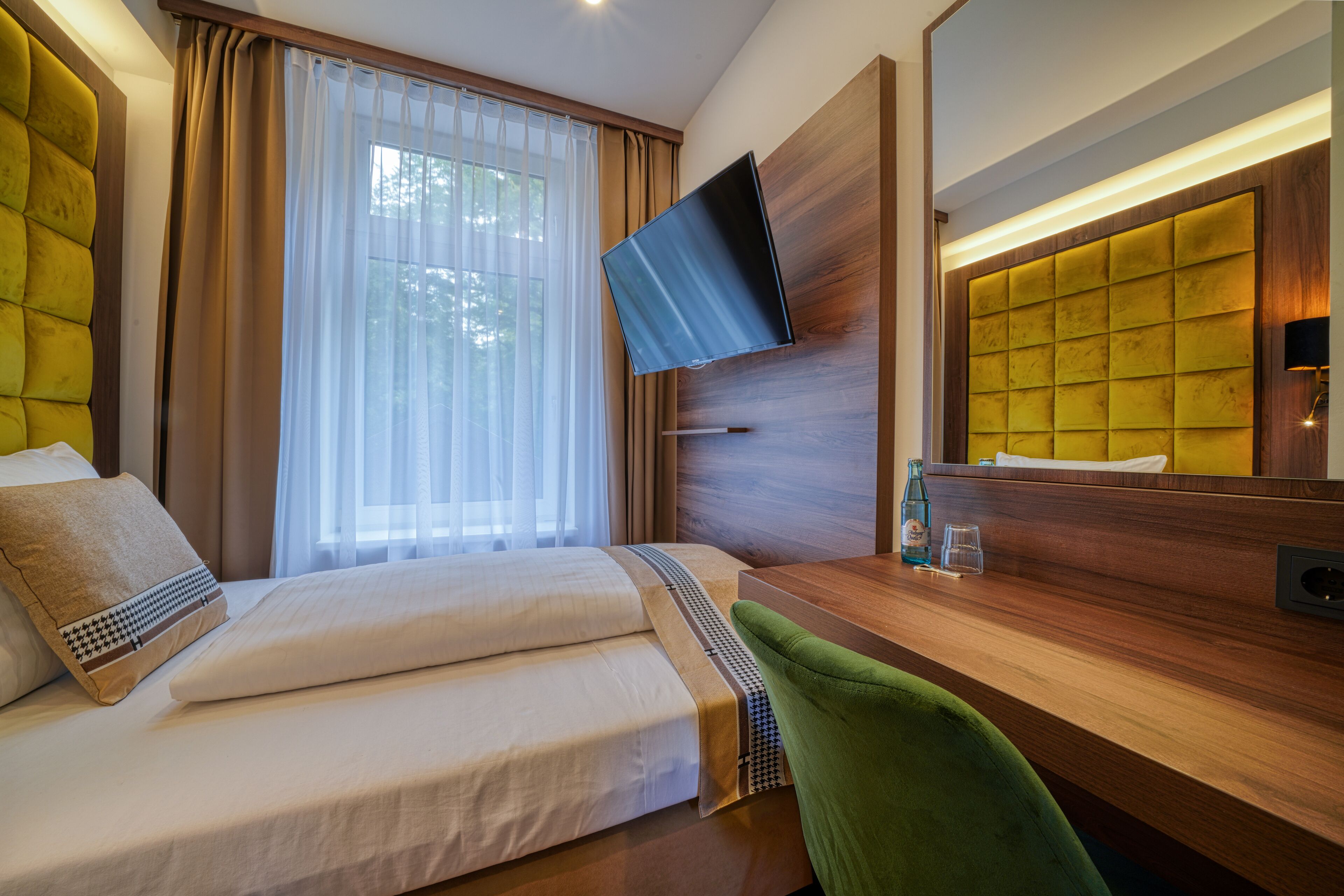 Ein Hotelzimmer mit Bett, Schreibtisch, Wandfernseher und einem Vorhangfenster.