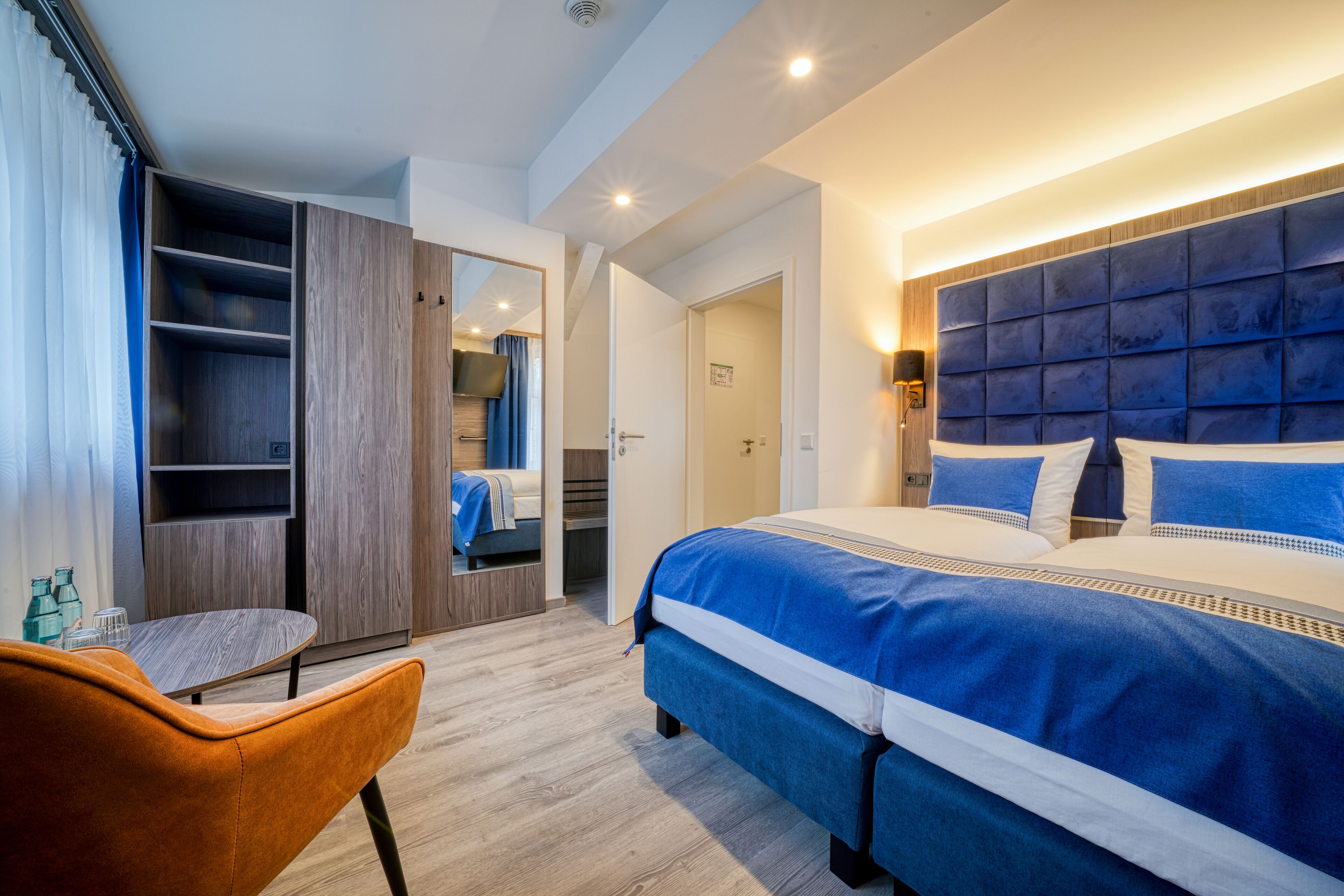Ein modernes Schlafzimmer mit einem großen Bett, einem Kleiderschrank, einer Sitzecke und einem durch eine offene Tür einsehbaren Badezimmer.