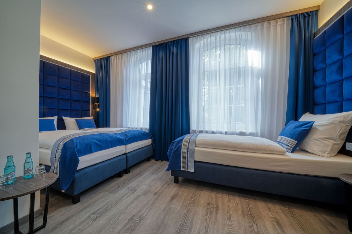 Habitación de hotel con dos camas, una mesita y una ventana con cortinas.