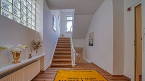 Un couloir d’hôtel avec un escalier en bois, un radiateur et une moquette jaune ornée du nom de l’hôtel.