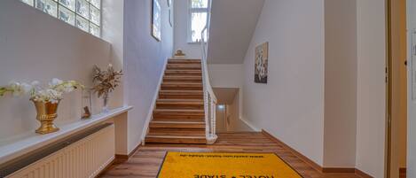 A hotel hallway with a wooden staircase, a radiator, and a yellow carpet with the hotel name.