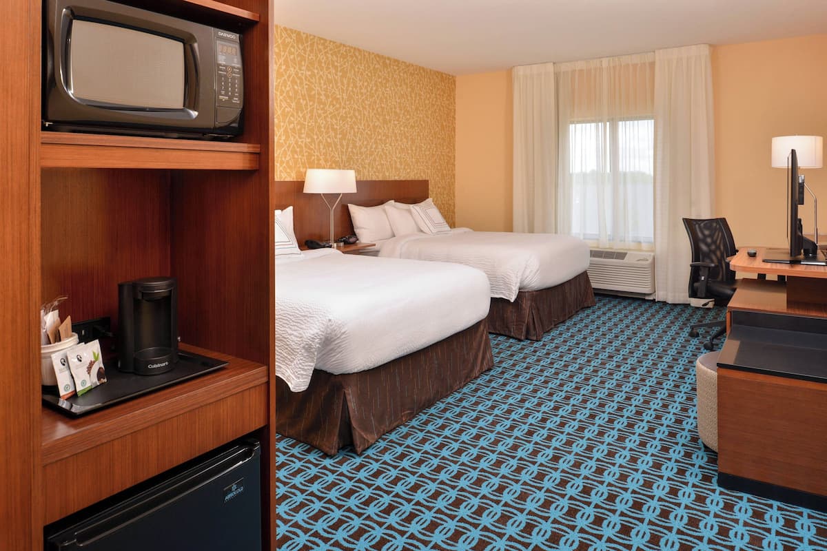 A hotel room with two beds, a minibar, a desk with a computer, and a large window with curtains.