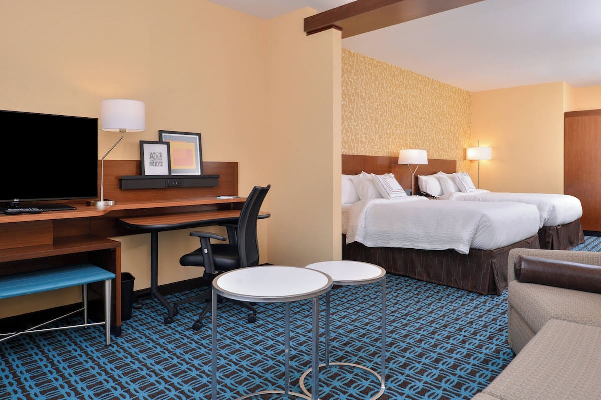 A hotel room with a bed, a desk, a chair, two small tables, a TV, and a patterned carpet.