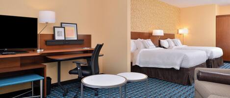 A hotel room with a bed, a desk, a chair, two small tables, a TV, and a patterned carpet.