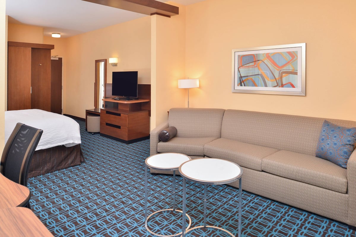 A hotel room with a bed, a sofa, two small tables, a TV, a lamp, and a framed picture on the wall.
