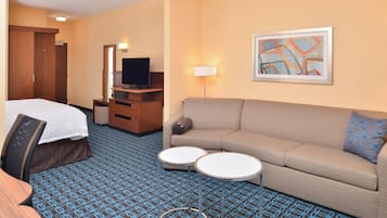 A hotel room with a bed, a sofa, two small tables, a TV, a lamp, and a framed picture on the wall.