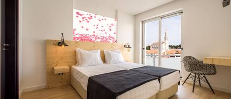 Un dormitorio con cama, mesitas de noche, una silla, una ventana con vista a una torre y cabecera de madera.