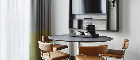 Une pièce moderne avec une table ronde, deux fauteuils en cuir, une machine à café et un téléviseur fixé au mur.