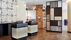 Un área de recepción con diseño moderno, que incluye un mostrador de madera, una pared con patrón geométrico y un cartel que indica la ubicación de la despensa.