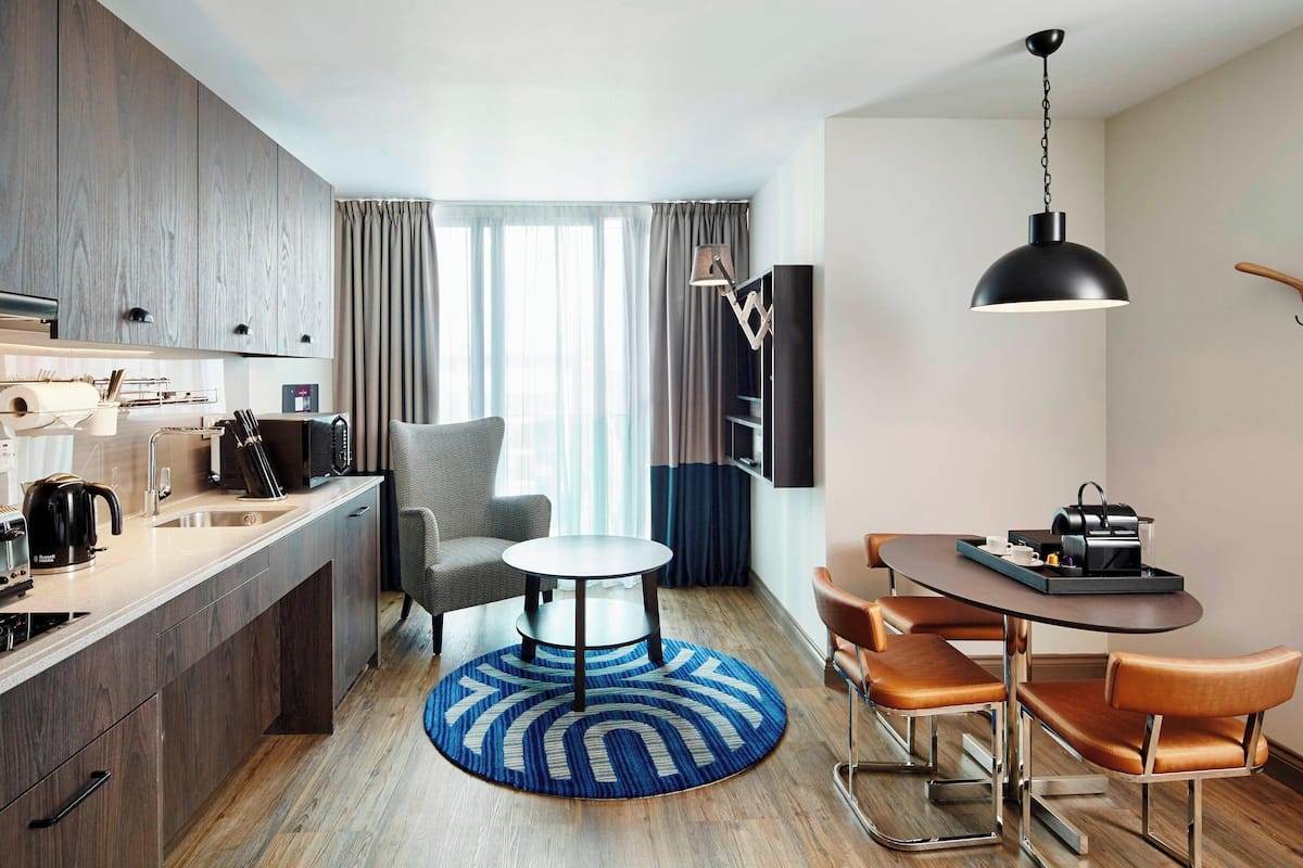 A modern kitchen with a dining area, featuring a round table, chairs, and a blue rug.