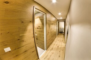 Un couloir aux murs et au sol en bois, qui mène à une pièce équipée d’un radiateur et d’un lit.