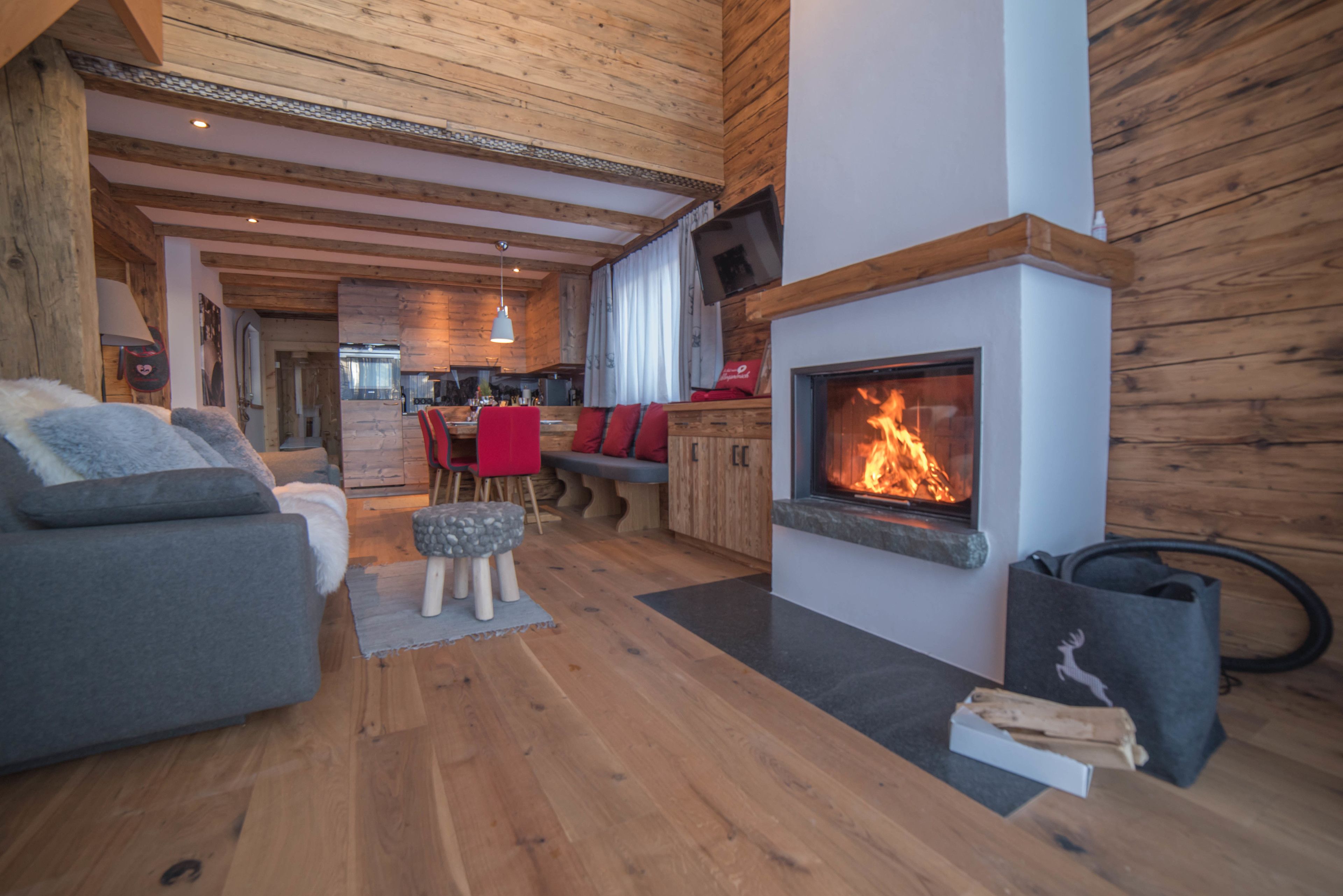 A cozy living room with a fireplace, wooden floors, and a dining area with red chairs.