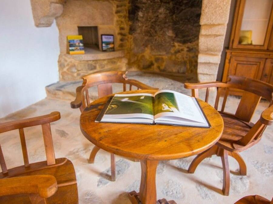 A round wooden table with an open book in the center, surrounded by wooden chairs.
