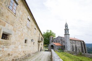 A stone building with a bell tower, a paved pathway, and a grassy area. - Monasterio y Pensión de Moraime (Muxía)