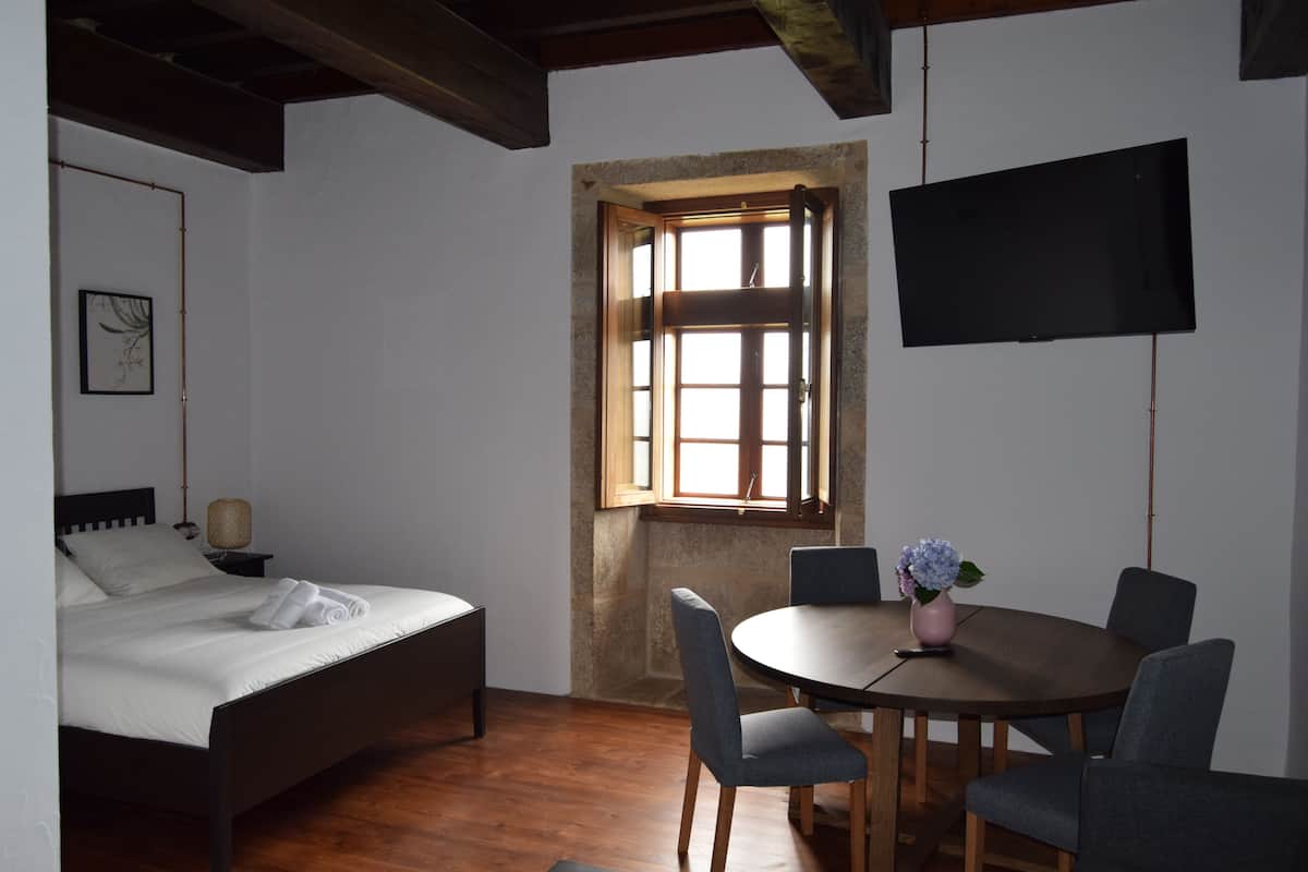Un dormitorio con cama, una mesa redonda con sillas, televisor y ventana con vista.