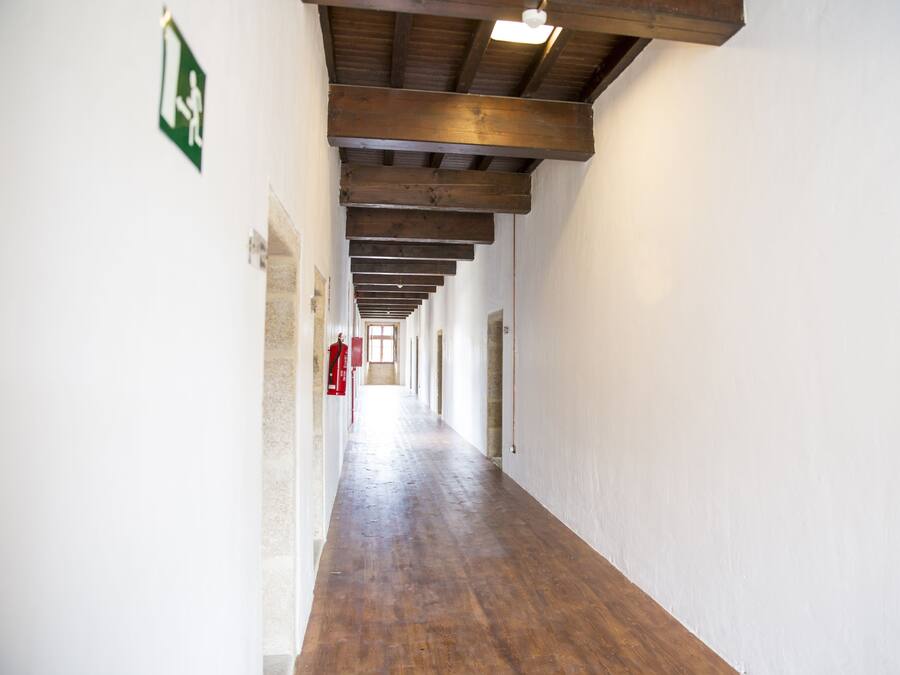 A long, narrow hallway with wooden beams on the ceiling and white walls.