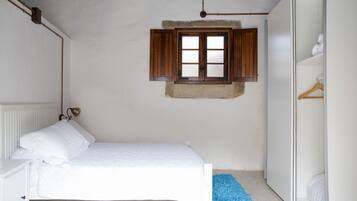 Een slaapkamer met een bed, een raam met houten luiken, een radiator en een kledingkast.