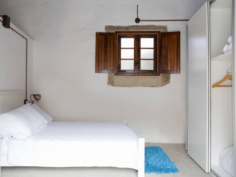 Een slaapkamer met een bed, een raam met houten luiken, een radiator en een kledingkast.