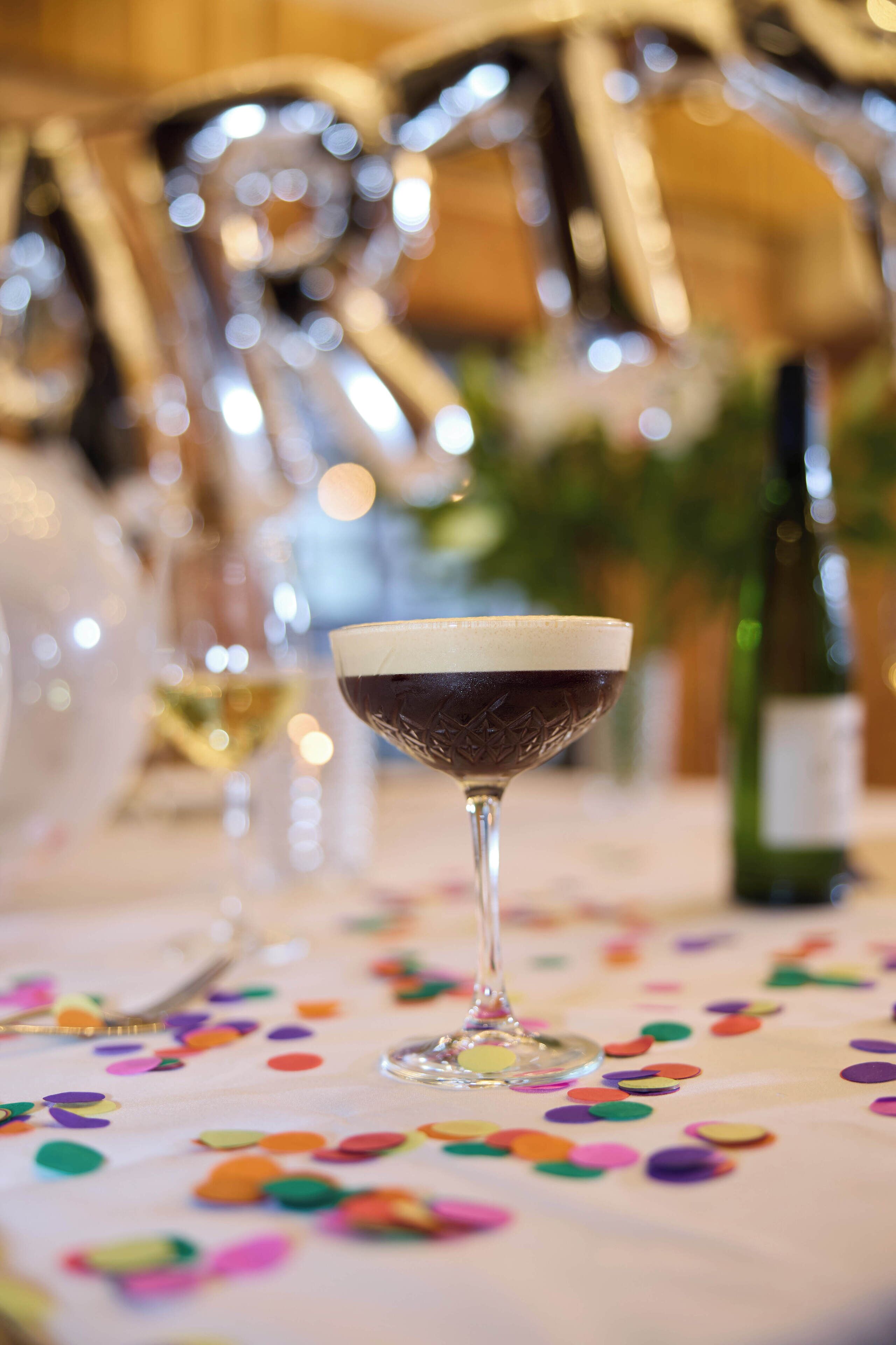 A table with a colorful tablecloth and a glass of dark-colored drink.