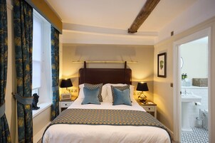 A bedroom with a large bed, two bedside tables with lamps, a window with curtains, and a view of a bathroom.