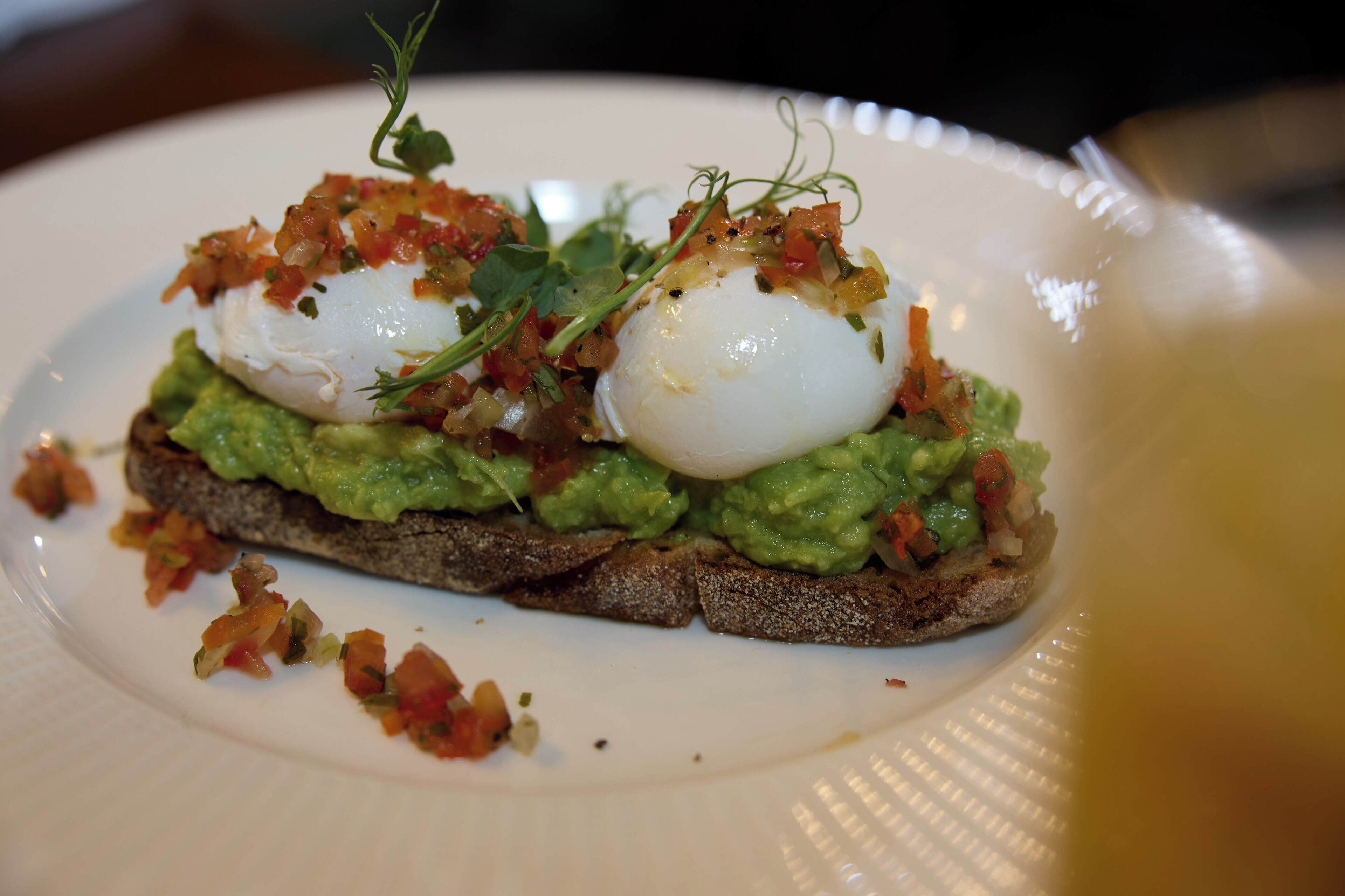 En tallrik med en smörgås, garnerad med avokado, pocherade ägg och en dekorativ detalj.
