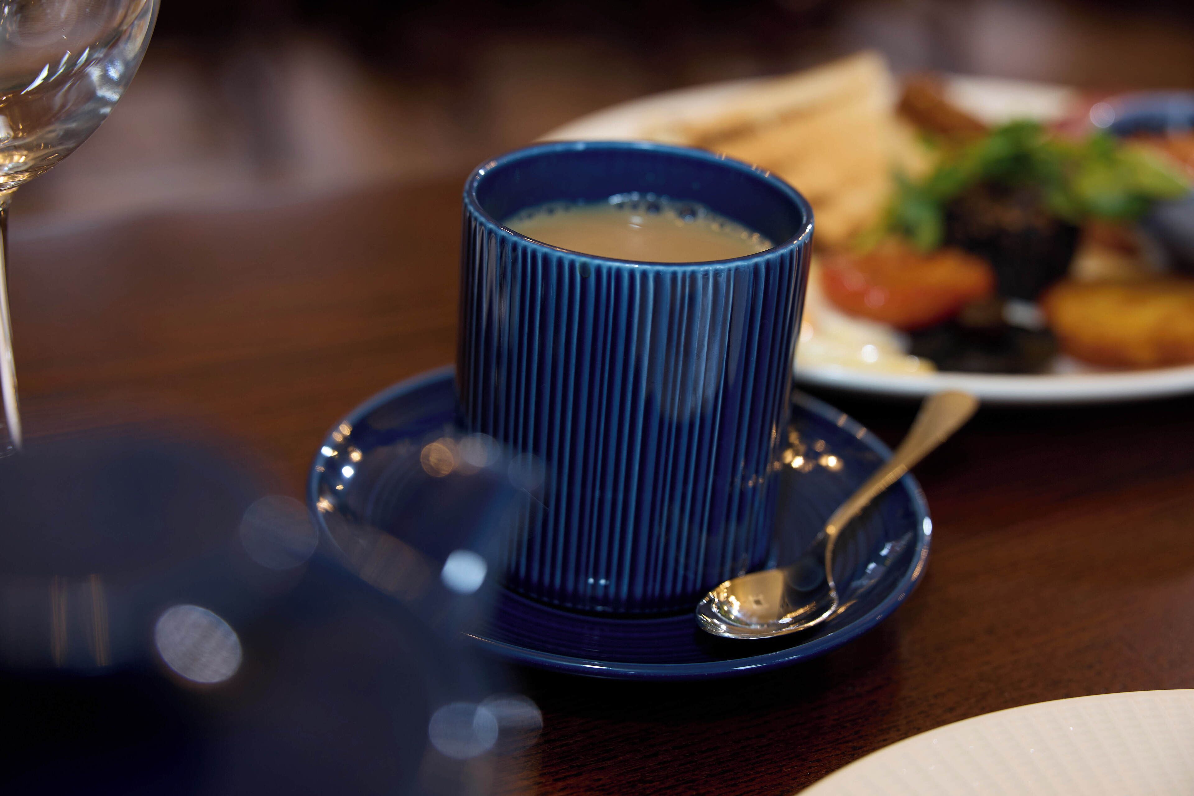 A table setting with a blue cup, a spoon, and a plate with food.