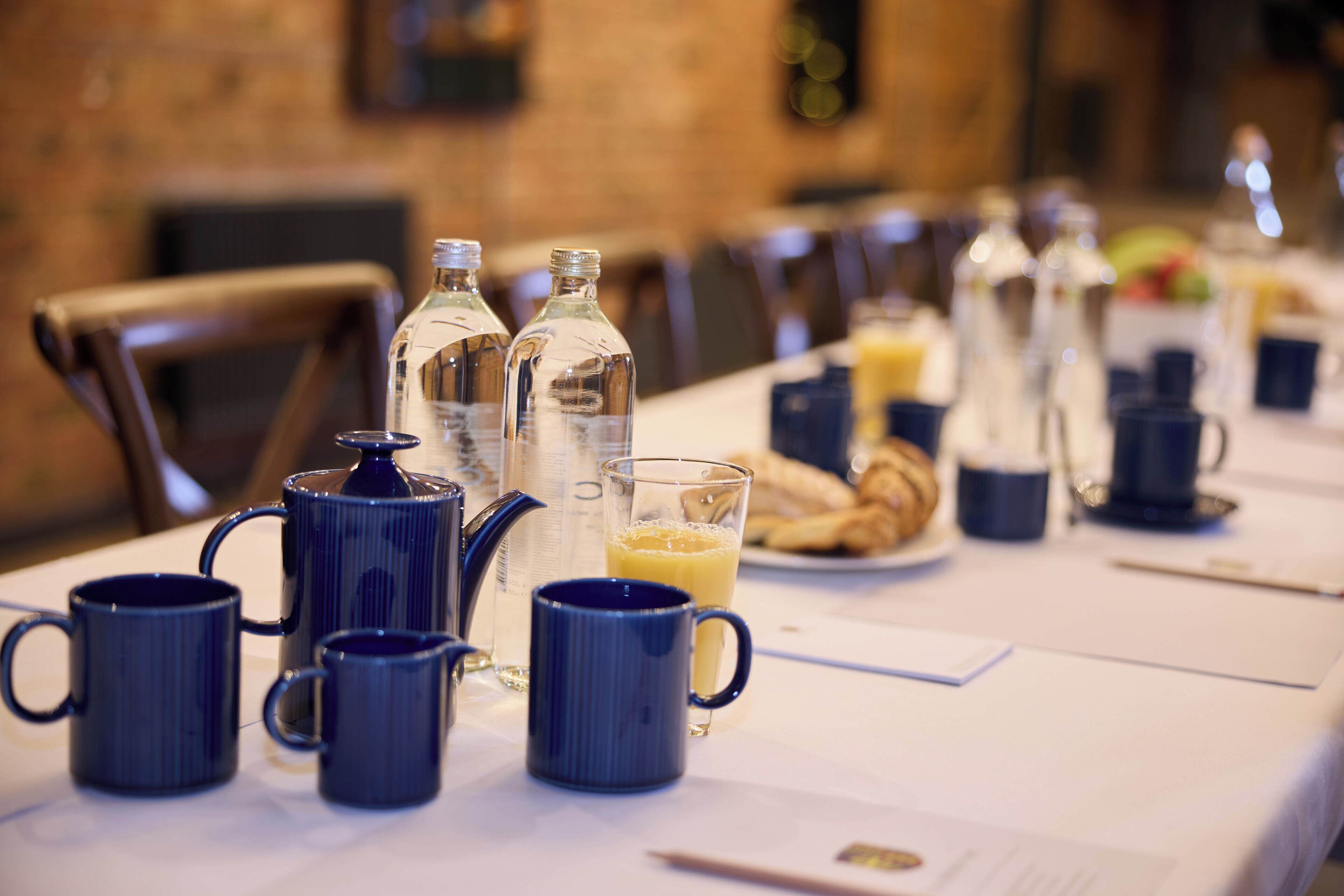 A breakfast table with blue mugs, a coffee pot, and a glass of orange juice.