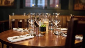 A dining table set with multiple wine glasses, a small potted plant, and neatly folded napkins. - The White Hart (Bedford)