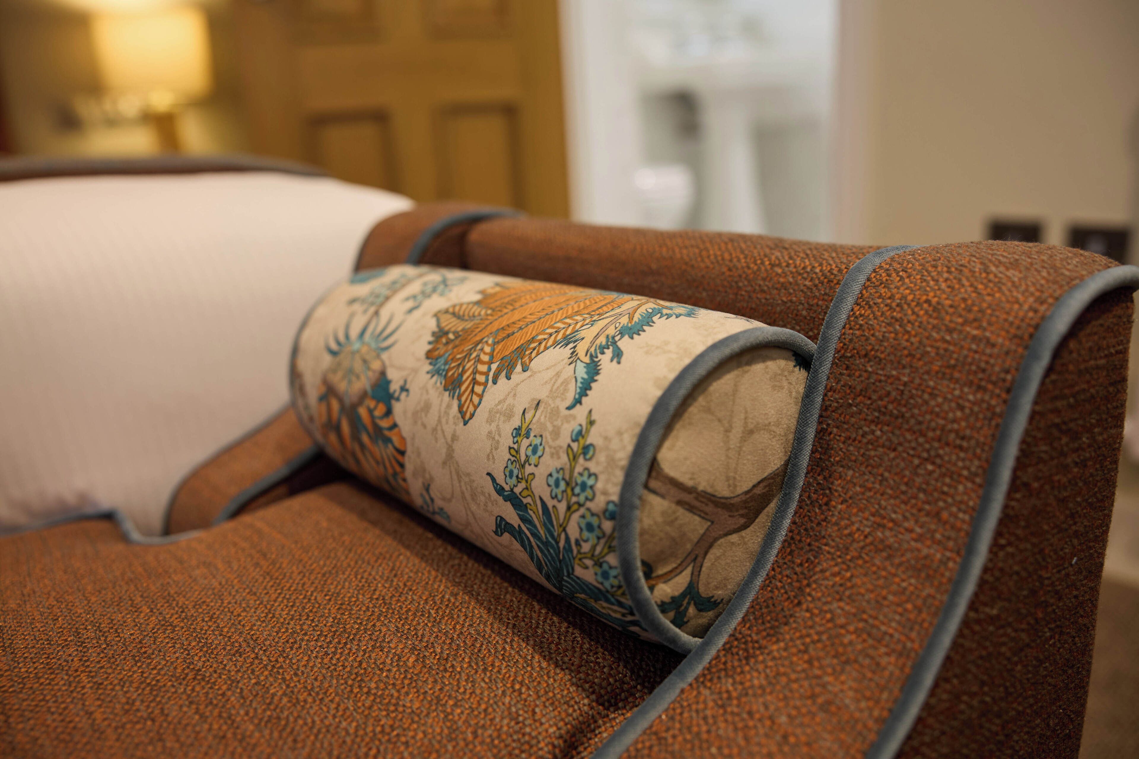 Primer plano de una butaca marrón tapizada con un cojín decorativo de estampado floral.