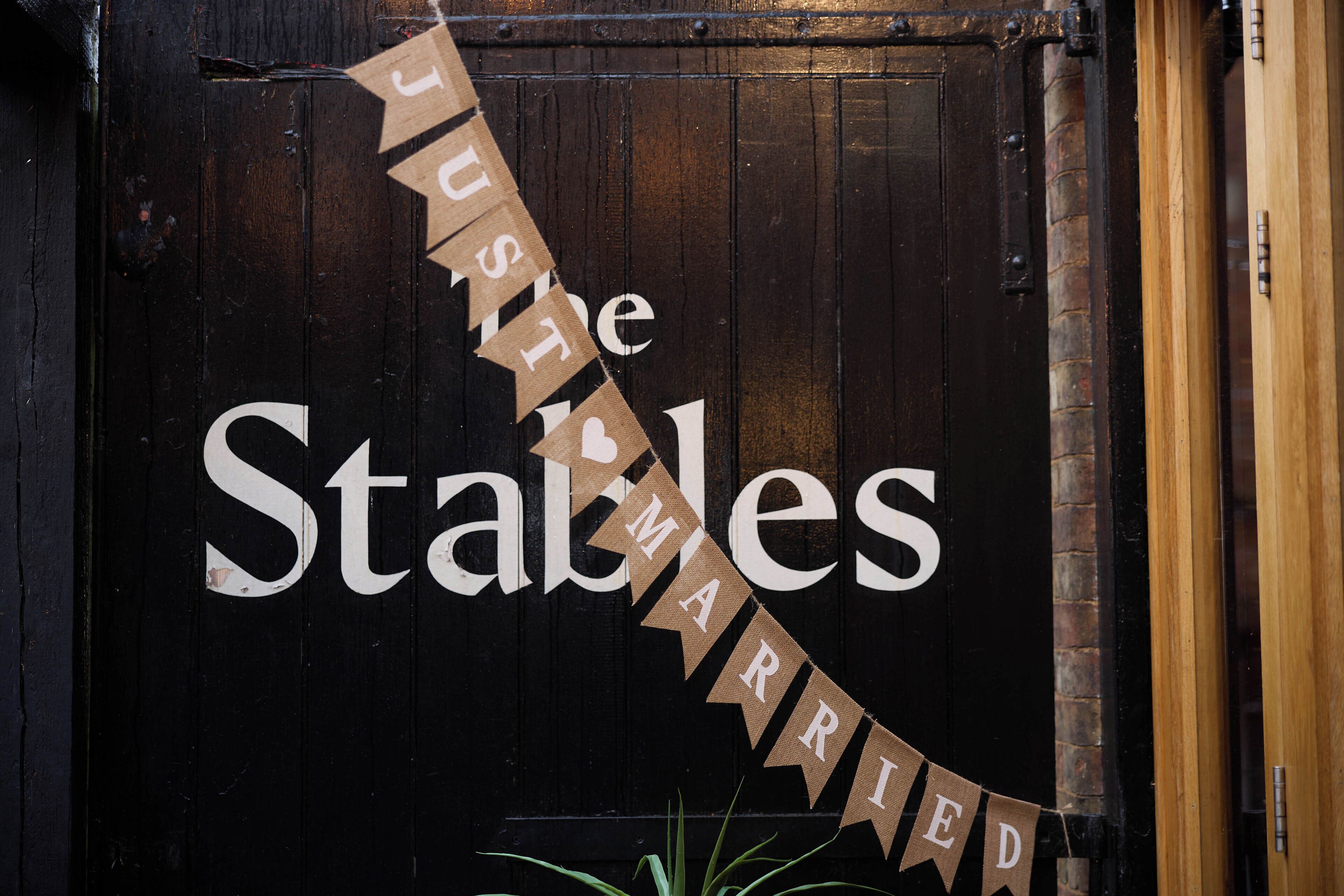 En trædør med et banner, der viser teksten "JUST THE STABLES MARRIED", og en lille plante forneden.