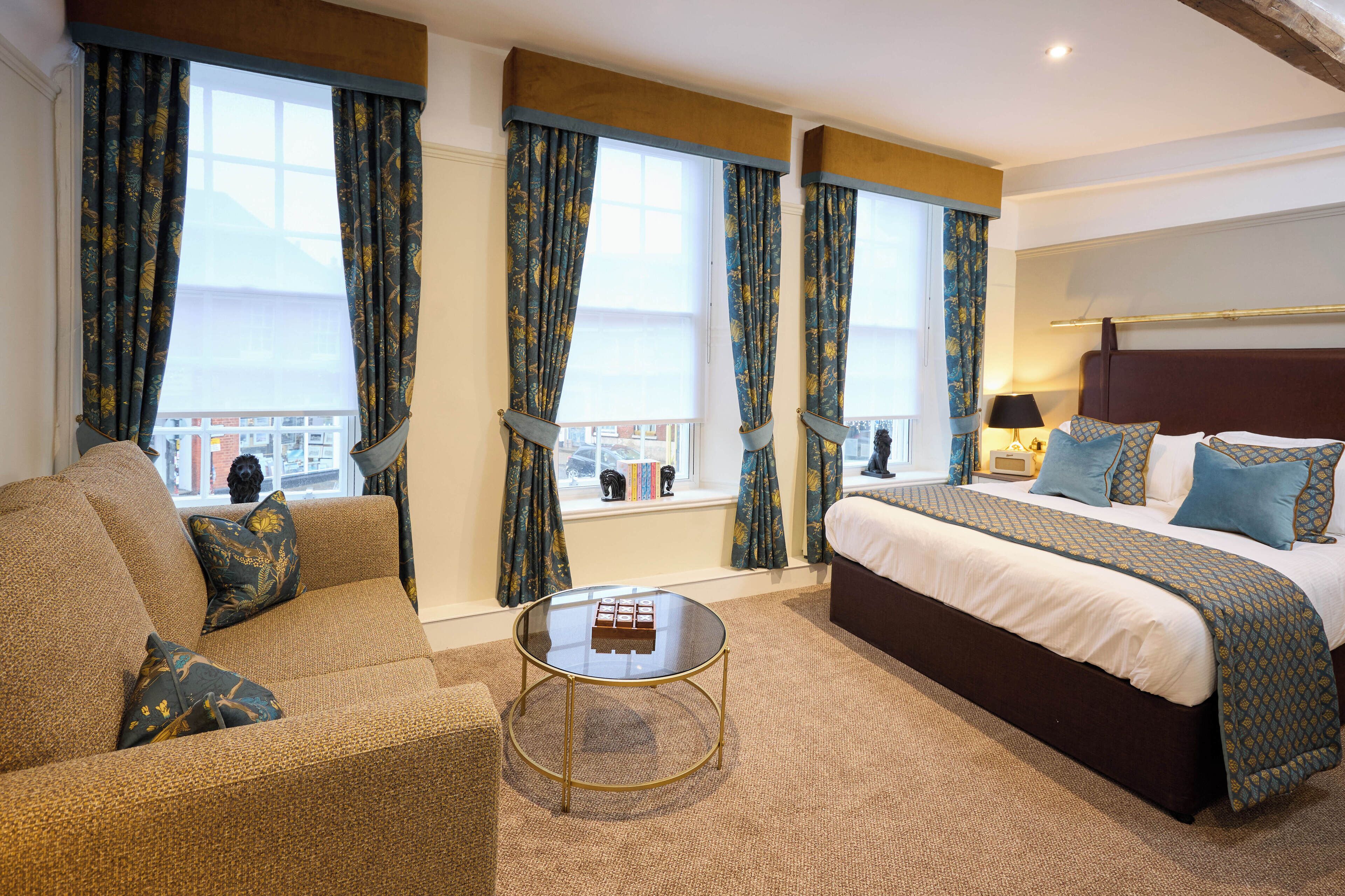 Een hotelkamer met een groot bed, een bank, een klein bijzettafeltje en gordijnen met een bloemenprint.