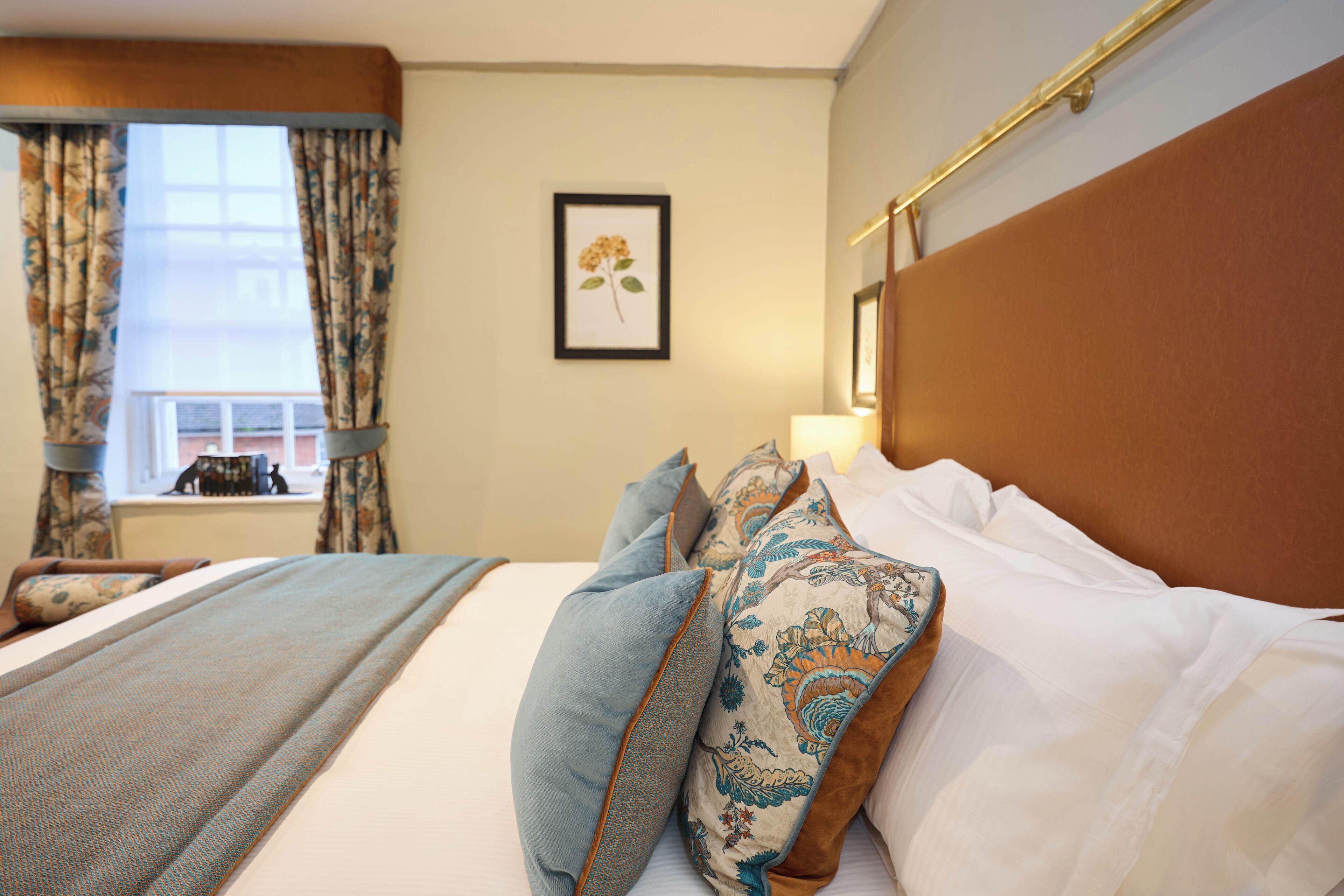 Quarto de hotel com uma cama grande, janela com cortinas, um quadro na parede e cabeceira.